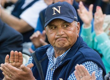 A man clapping in a crowd wearing a blue vest, blue gingham shirt and cap with an N on it. Photo of Peter Tosi '66, at his 50th Reunion, Homecoming 2016.