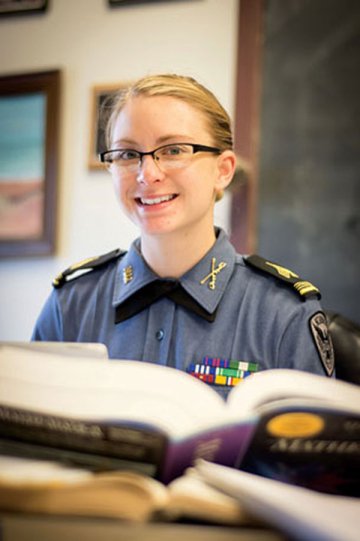A young woman in formal military shirt smiles as photographed behind an open book at a desk. Photo of Rebecca Sweem '16, NUCC Regimental Commander 2015-2106.