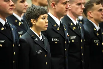 A woman stands among men, fellow graduates in navy blue formal military attire. Photo of Terry Atwater, '16.