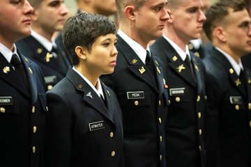A woman stands among men, fellow graduates in navy blue formal military attire. Photo of Terry Atwater, '16.