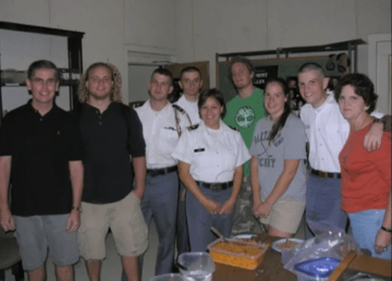 Group of students stand before a table with food. Video still from "Thanks for making the Norwich Forever! campaign a success."