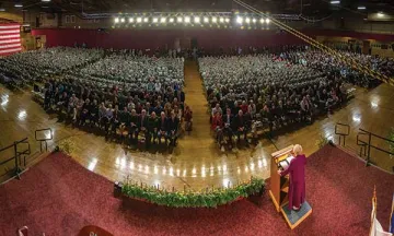 In a view from above, a woman in red dress at a lectern addresses a standing room only crowd. Photo of US Secretary of State Madeleine Albright on US election day, 11/3/2015.