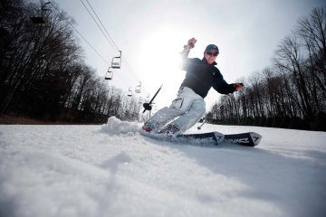 skier in white snow pants and black fleece jacket and hat, with ski poles up, turning to his left