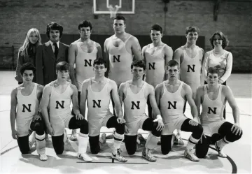 Black and white photo of ten young men in wrestling uniforms with an N on center front, six kneeling front row, four standing back row, with a woman, man and younger woman standing on either side of the four. Norwich University wrestling team 1976.