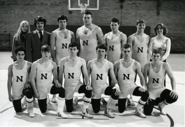 Black and white photo of ten young men in wrestling uniforms with an N on center front, six kneeling front row, four standing back row, with a woman, man and younger woman standing on either side of the four. Norwich University wrestling team 1976.