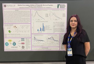 Student stands beside a Norwich University research poster at a conference.