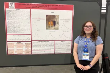 Student stands beside a Norwich University research poster on xanthophyll extraction from bacteria.