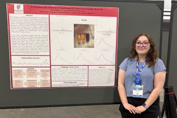 Student stands beside a Norwich University research poster on xanthophyll extraction from bacteria.