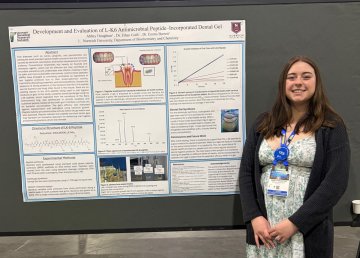 Student stands beside a Norwich University research poster on antimicrobial peptide dental gel.