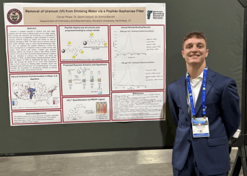Student stands beside a research poster on removing uranium from drinking water with a peptide filter.