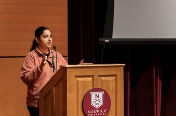 Student speaks at a podium with a Norwich University seal on stage.