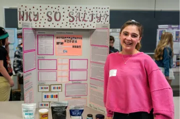 Student stands beside a science fair display titled "Why So Salty?"