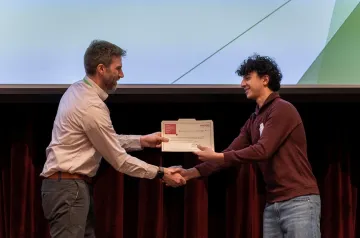Person shakes hands with a student receiving a certificate on a stage.