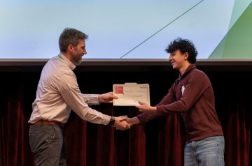 Person shakes hands with a student receiving a certificate on a stage.