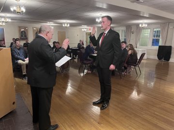 A man raises his right hand during an oath while another man reads from a paper at a podium.