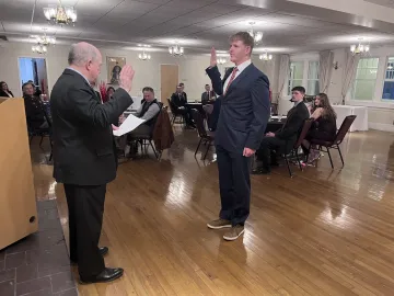 A man raises his right hand during an oath while another man reads from a paper at a podium.