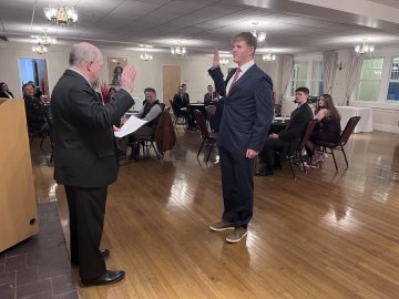 A man raises his right hand during an oath while another man reads from a paper at a podium.