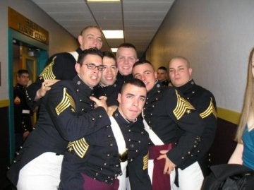 Seven individuals in formal military attire huddle close together in a hallway.