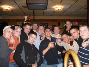 Group of individuals huddle close together indoors, some holding beverages in glasses or mugs.