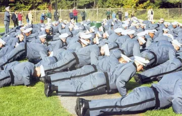 Large group of individuals in grey formal military uniform doing pushups.