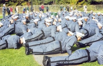 Large group of individuals in grey formal military uniform doing pushups.