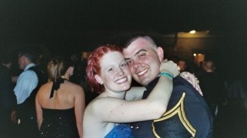 Two smiling individuals in formal attire embrace indoors.
