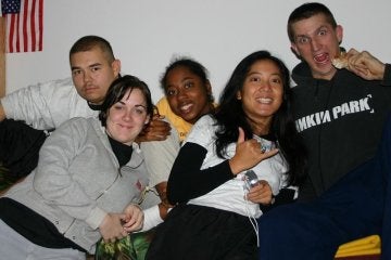 Five individuals sitting together smiling before a white wall and small US flag frame right.