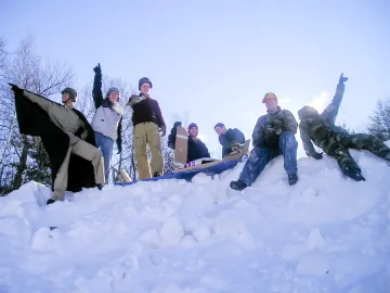 Individuals outdoors on a snowbank, several raising their arms in the air.