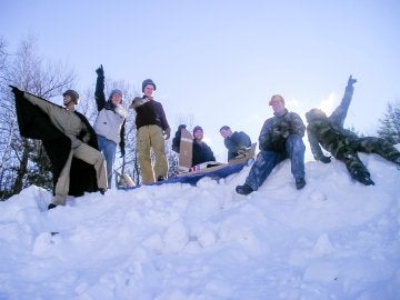 Individuals outdoors on a snowbank, several raising their arms in the air.