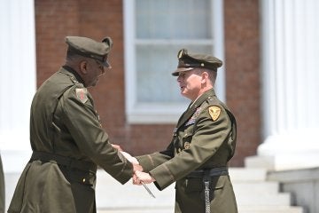 Two uniformed officers shake hands during an outdoor military ceremony.