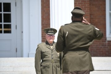 One uniformed officer salutes another during an outdoor military ceremony.