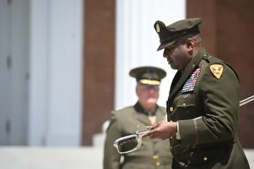 Uniformed officer holds a ceremonial sword during an outdoor military ceremony.