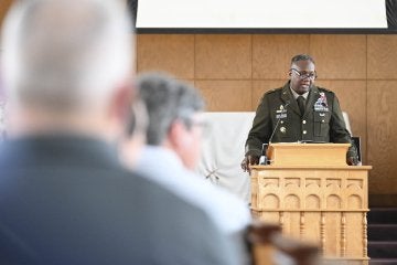 Uniformed officer speaks at a podium while audience members listen indoors.