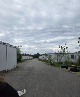 A paved road runs between rows of modular buildings under a cloudy sky.