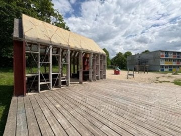 Wooden deck surrounds a partially built wooden shelter with apartment buildings in the background.