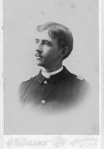 Service member in a dark uniform poses in profile for a studio portrait.