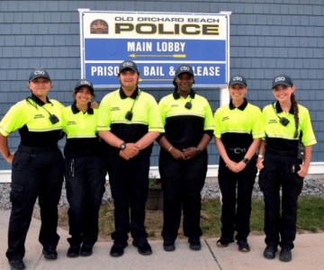 Six people in matching shirts and caps stand outside the Old Orchard Beach Police station.
