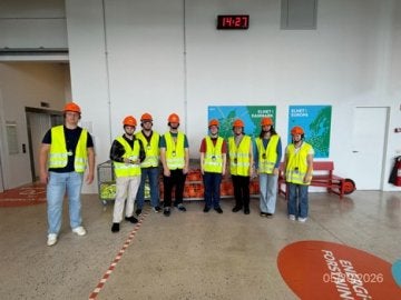 Eight people in safety vests and hard hats stand inside an industrial facility.