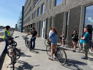 People stand with bicycles beside a modern building during a city bike tour.