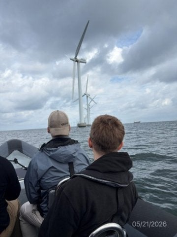 Two people ride in a boat toward offshore wind turbines.
