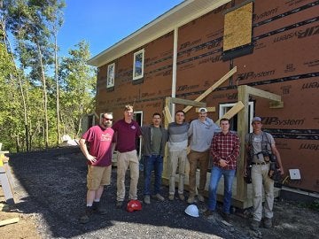 Seven people pose together in front of a building under construction.
