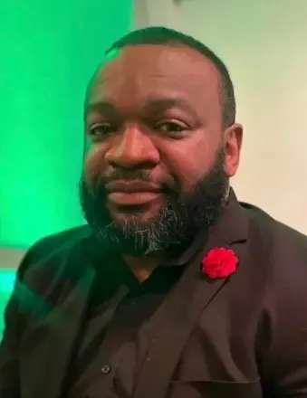 raheem Berry in a black shirt and suit portrait style.