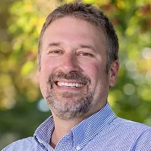 A headshot of a smiling man outdoors.