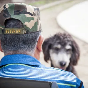 A man looks down at a dog in front of his chair.
