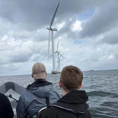 Two people ride in a boat toward offshore wind turbines.