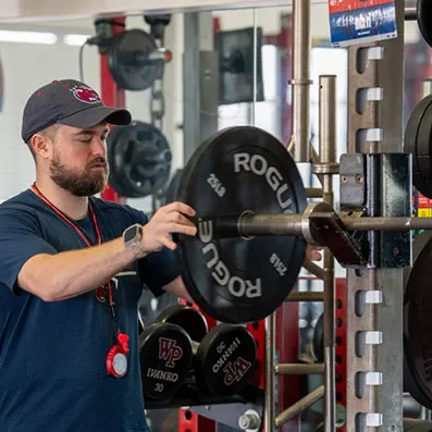A person places a weight plate on a barbell in a gym.