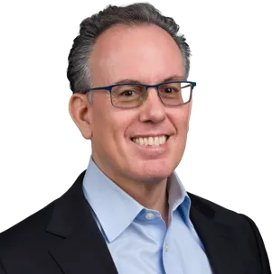 Portrait of a person wearing glasses, a dark blazer, and a light blue collared shirt.