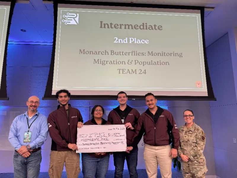 Norwich team at Rowdy Datathon holding their 2nd place prize in front of a sign that says "Intermediate 2nd Place - Monarch Butterflies: Monitoring Migration & Population (Team 24)"