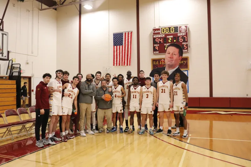 Norwich University 2025 Men's Basketball Team and Coaches celebrating head coach Paul Booth's 400th-career victory.