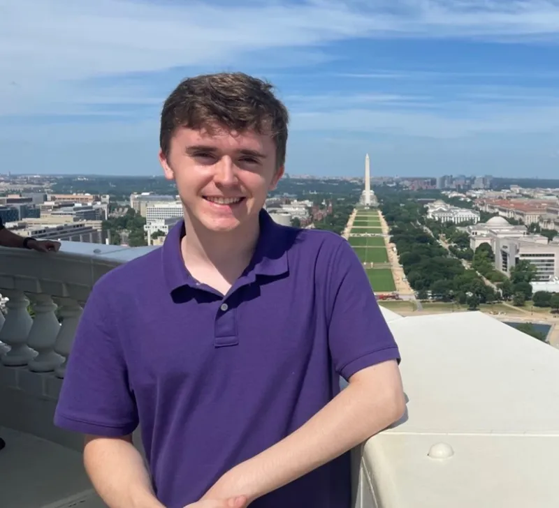Spencer Rada stands on a balcony overlooking the National Mall with a view of the Washington Monument.